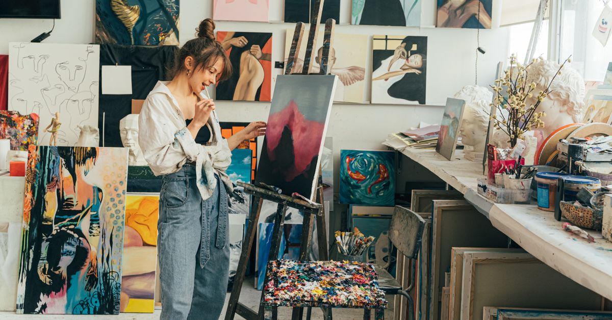 A young woman artist painting on canvas in her vibrant art studio filled with inspiring artworks.